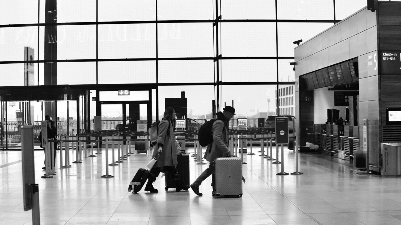 People walking through a bright, modern airport terminal with luggage and rolling bags