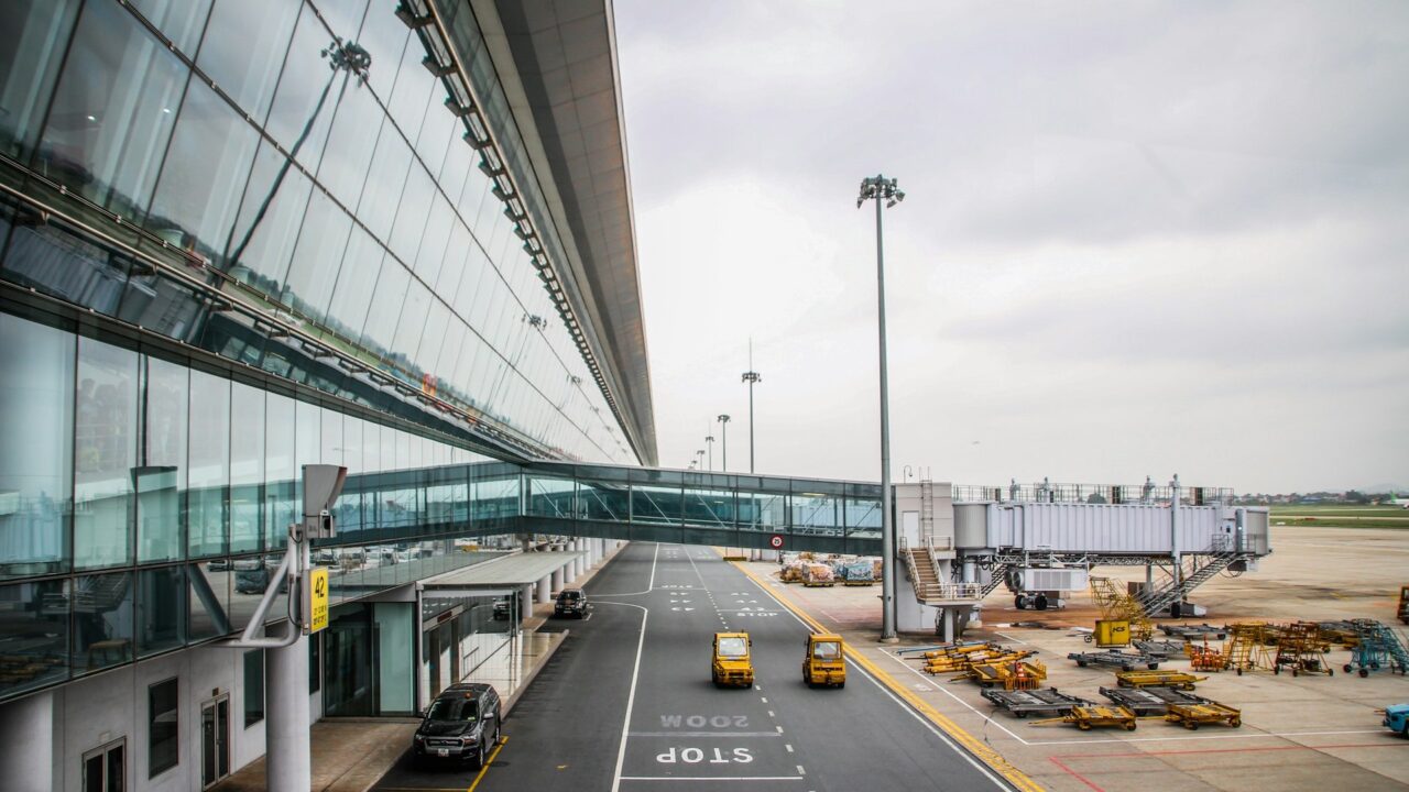 Vehicles on a road near a glass-fronted airport terminal building