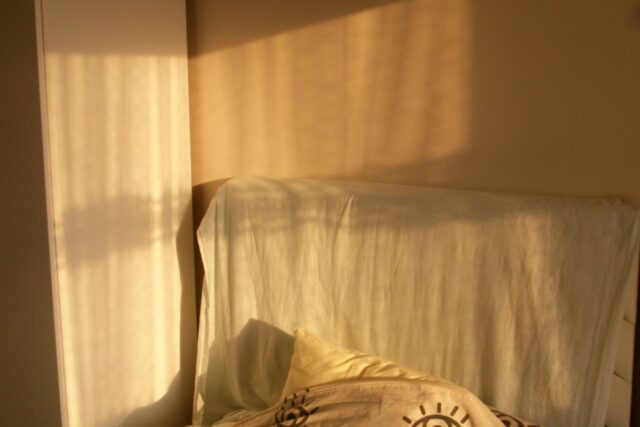Sunlit bedroom with unmade bed and sheer curtains casting shadows on walls