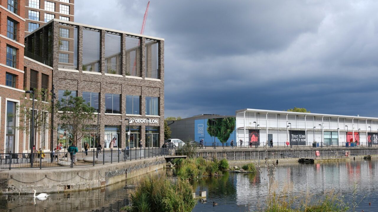 Modern residential and commercial buildings beside a waterway in an urban UK setting under cloudy skies
