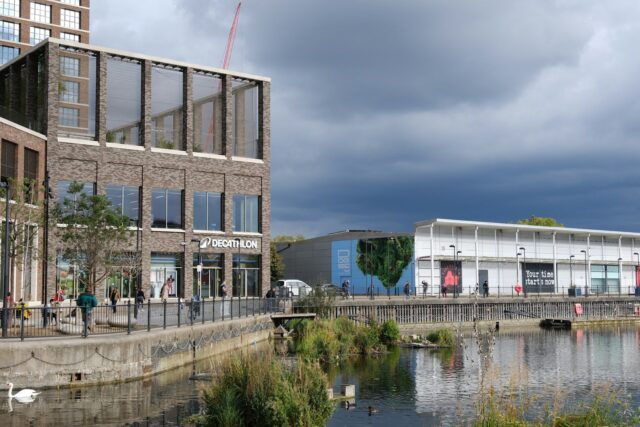 Modern residential and commercial buildings beside a waterway in an urban UK setting under cloudy skies