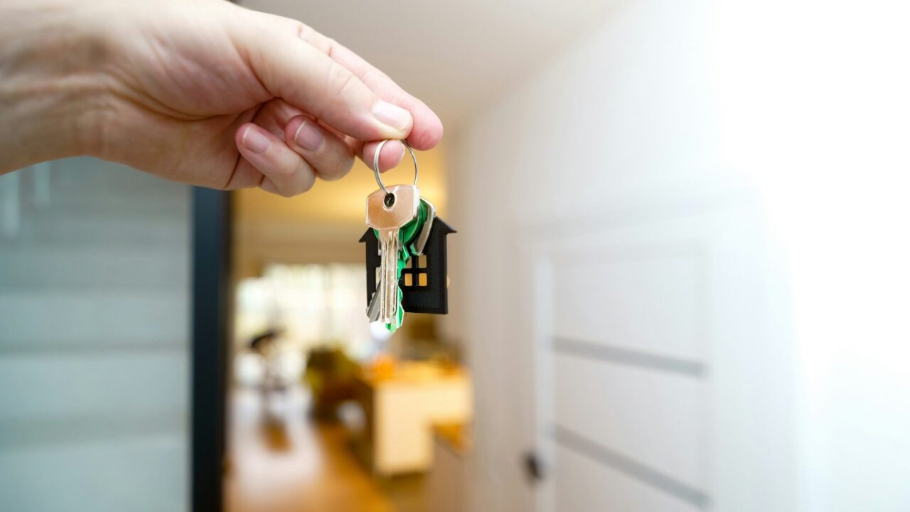 A hand holding house keys in front of a residential door entrance