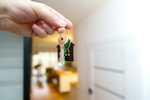 A hand holding house keys in front of a residential door entrance