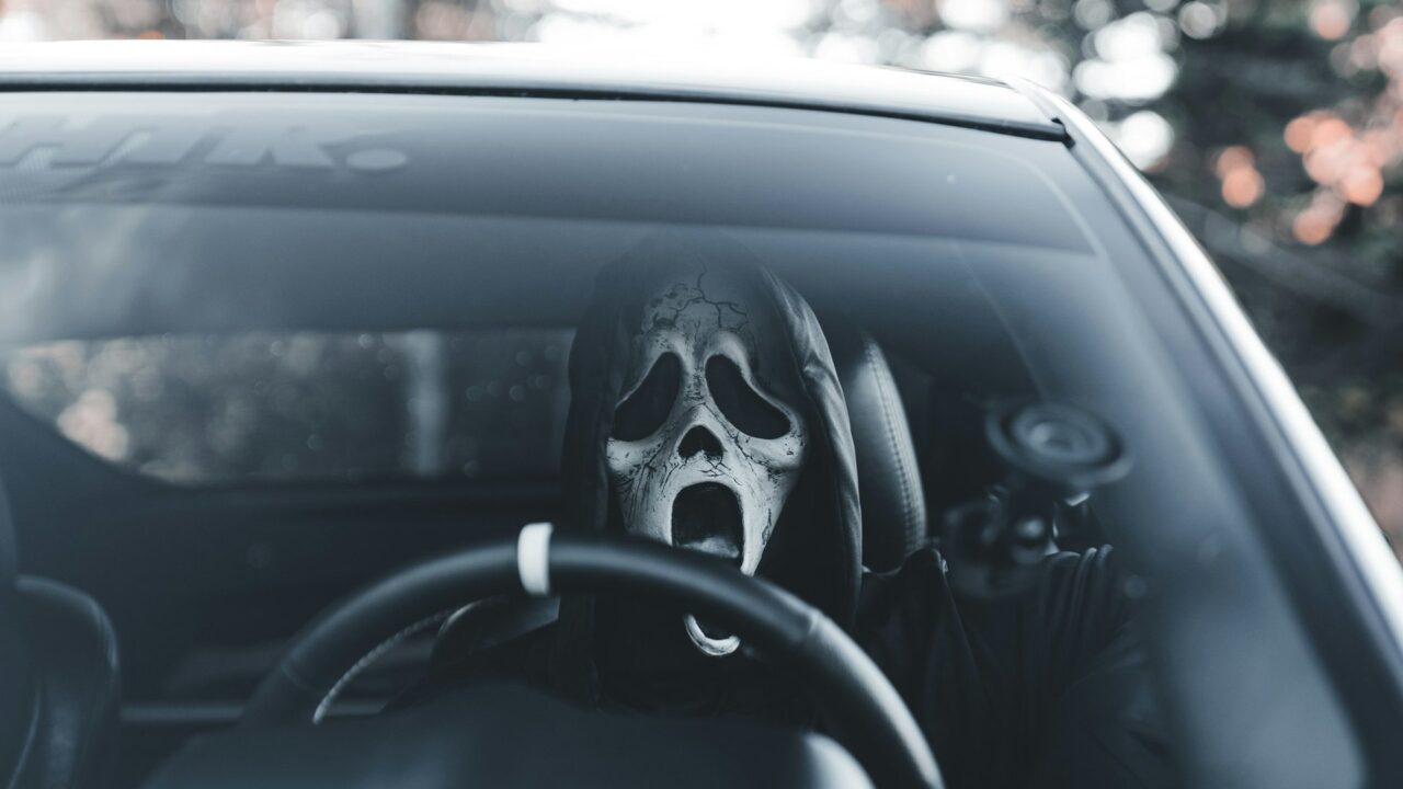 A skull mask positioned on a car's steering wheel viewed from inside the vehicle