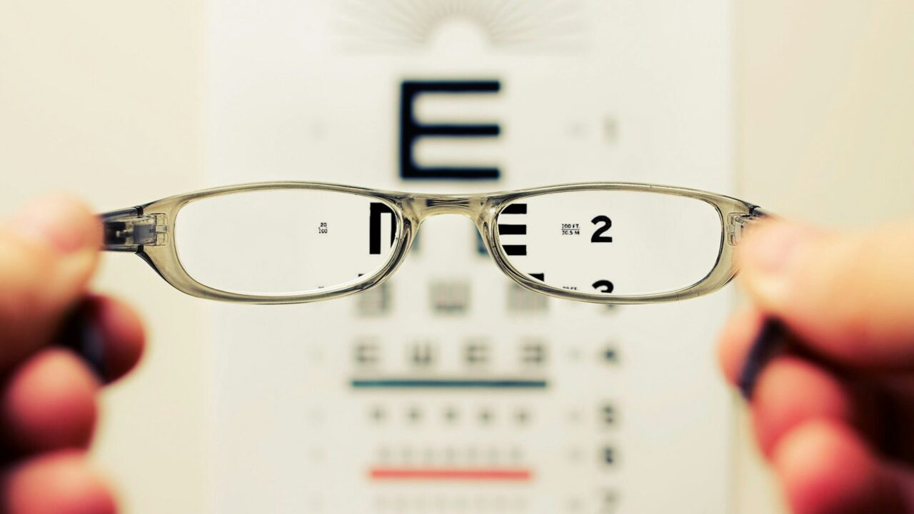 Pair of eyeglasses held up in front of an eye test chart