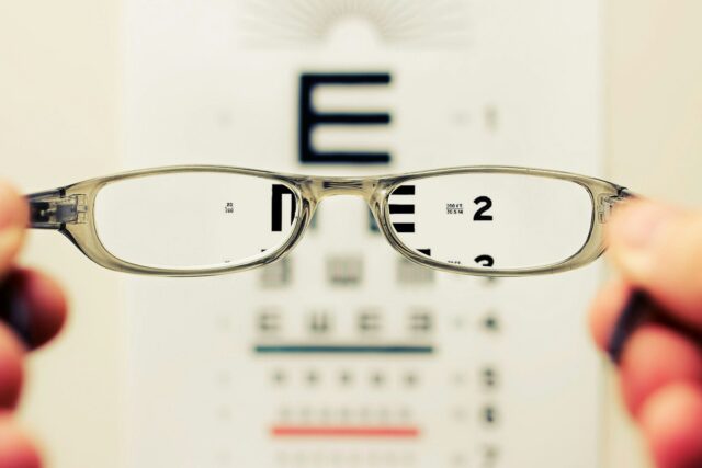 Pair of eyeglasses held up in front of an eye test chart