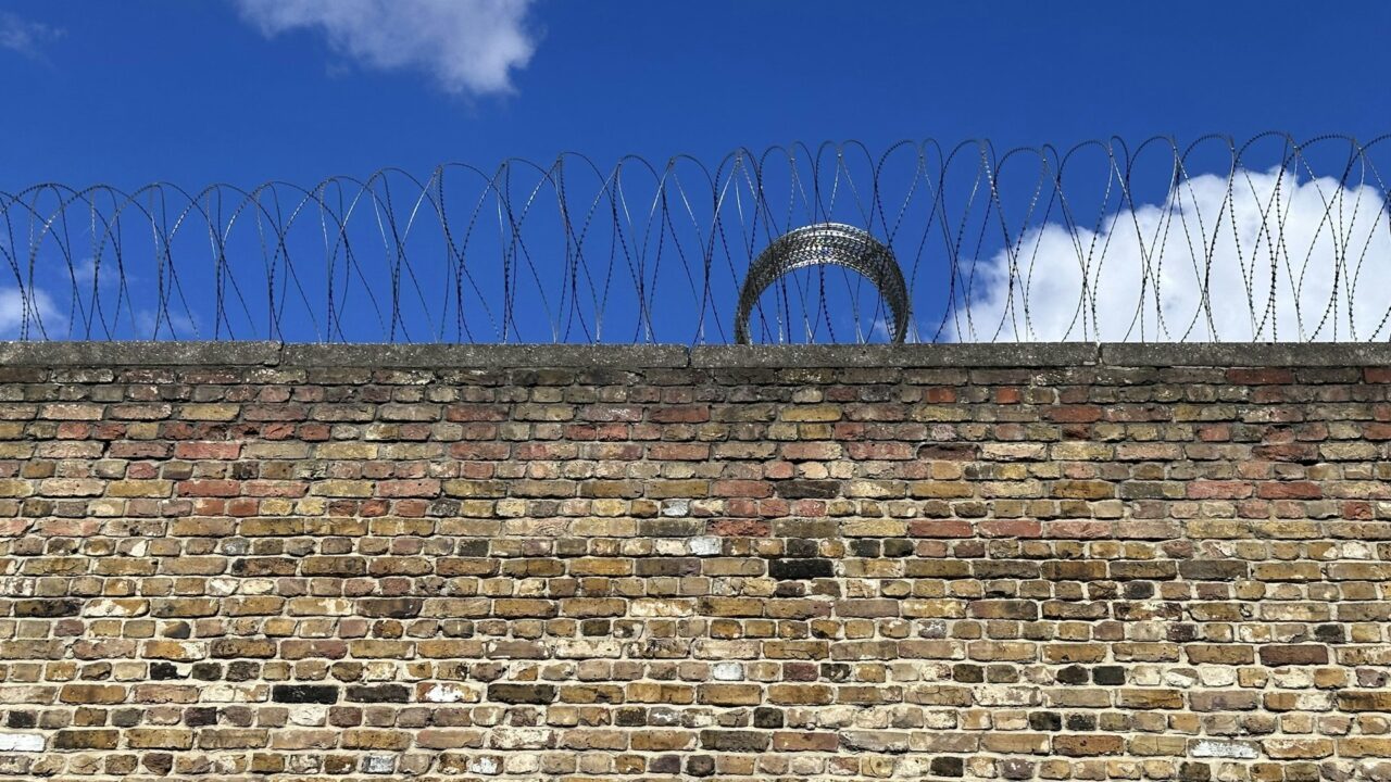 Brick wall topped with barbed wire against a blue sky, representing prison security.