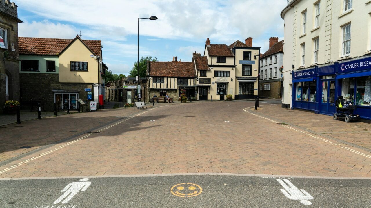A quiet British high street with period buildings, some appearing closed or vacant, representing a typical town centre