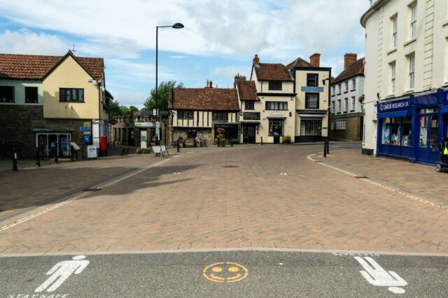 A quiet British high street with period buildings, some appearing closed or vacant, representing a typical town centre