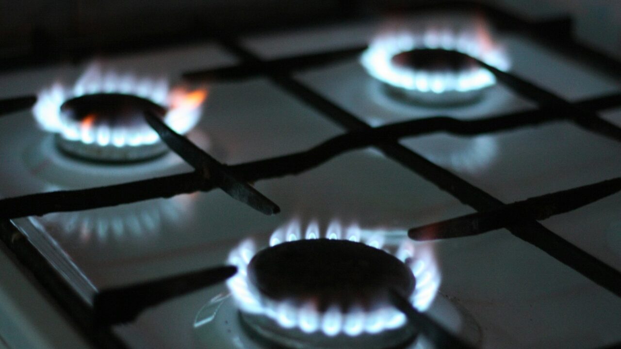 Close-up of three lit gas burners on a domestic cooktop, showing blue flames against black surface