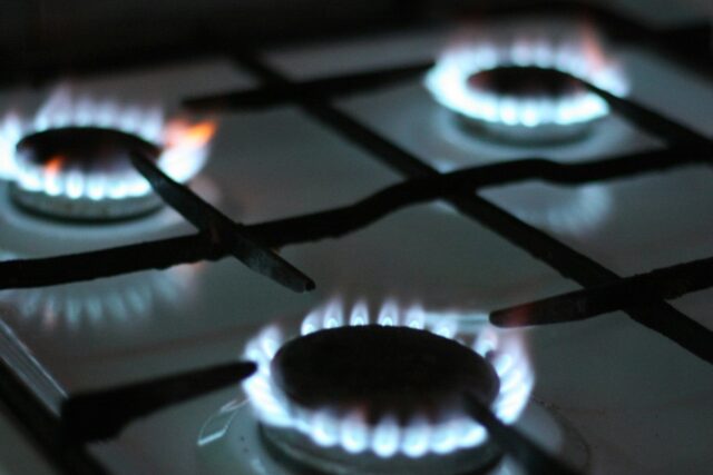 Close-up of three lit gas burners on a domestic cooktop, showing blue flames against black surface
