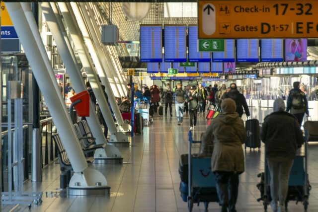 People walking through an airport terminal with flight information displays overhead