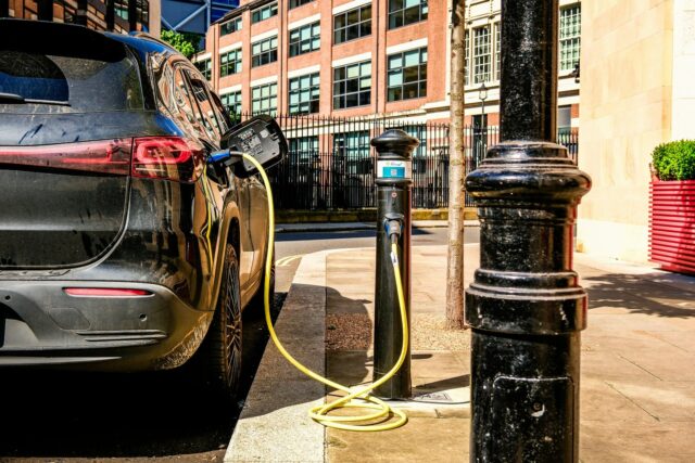 Electric vehicle plugged into a street-mounted charging station on an urban pavement