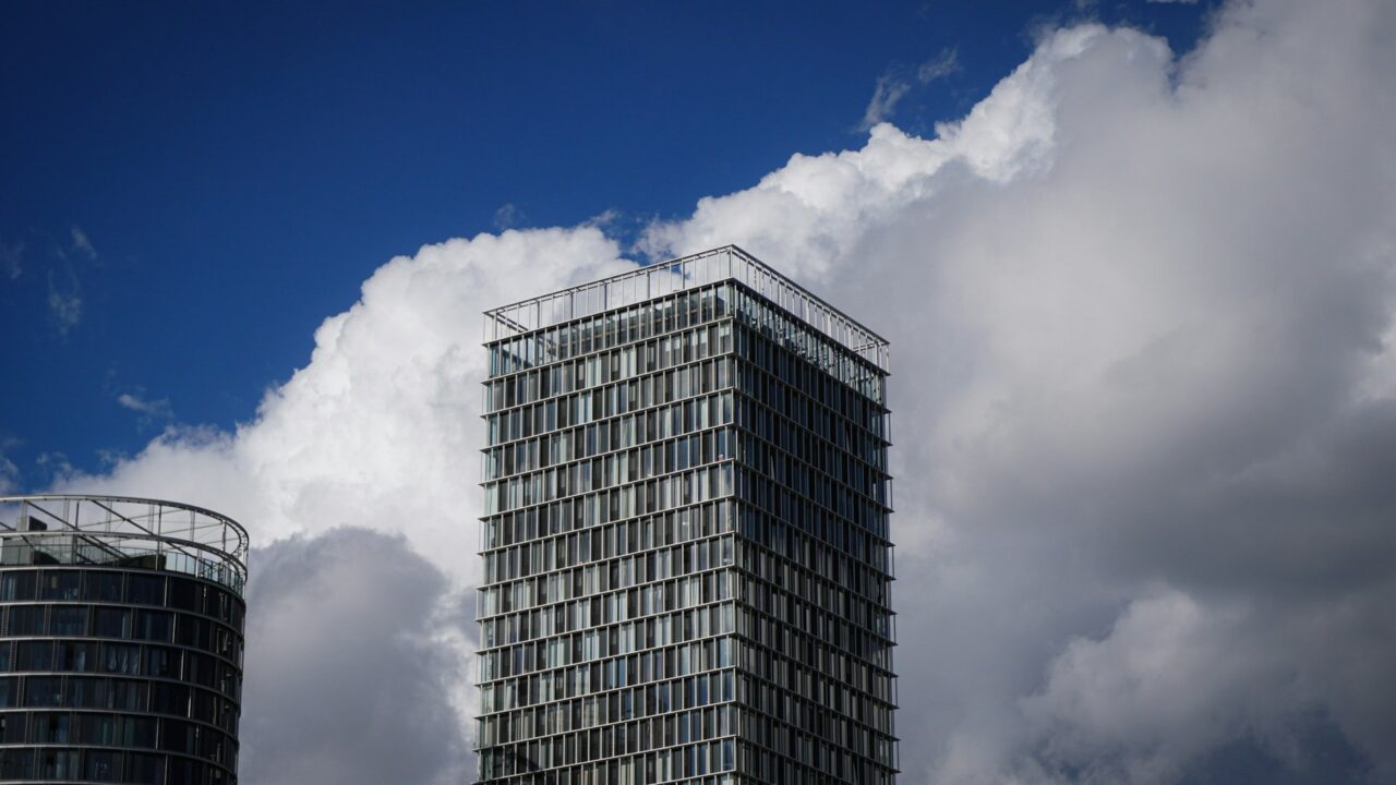 A tall modern office building with regular window pattern against a blue sky with white clouds