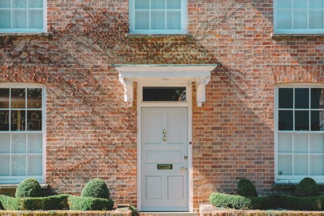 Brown brick residential building with white wooden door, blue-framed windows and potted plants