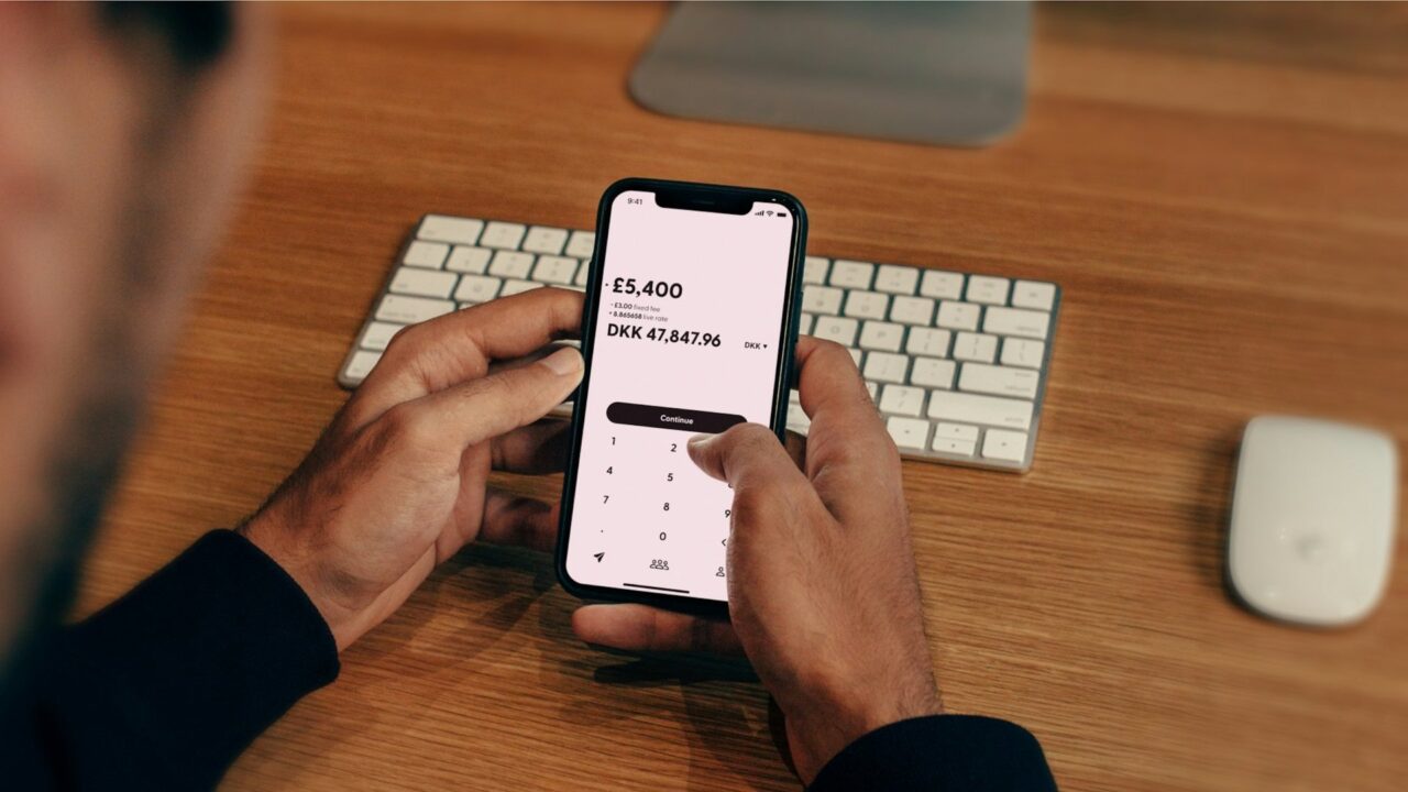 Person holding a smartphone displaying a banking app interface at a desk with keyboard