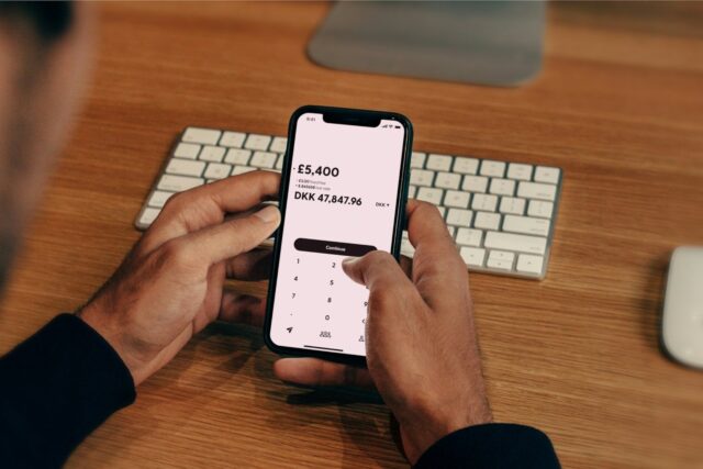 Person holding a smartphone displaying a banking app interface at a desk with keyboard