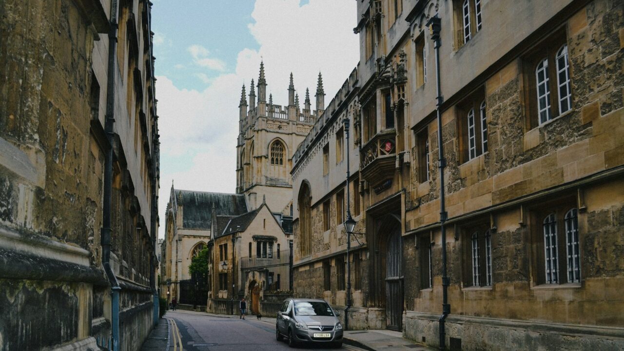 Cars parked along a historic stone street lined with traditional buildings in a UK town