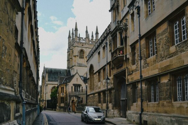 Cars parked along a historic stone street lined with traditional buildings in a UK town