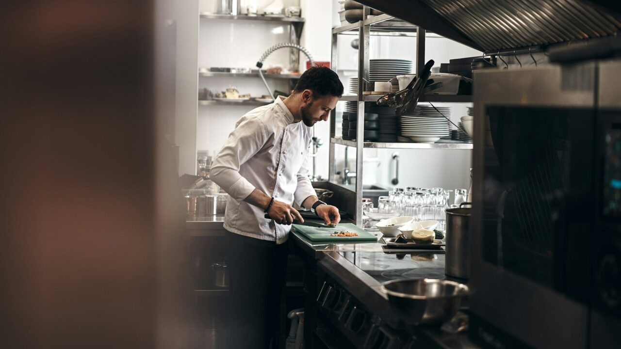 Chef in white coat chopping vegetables on a cutting board in a professional kitchen