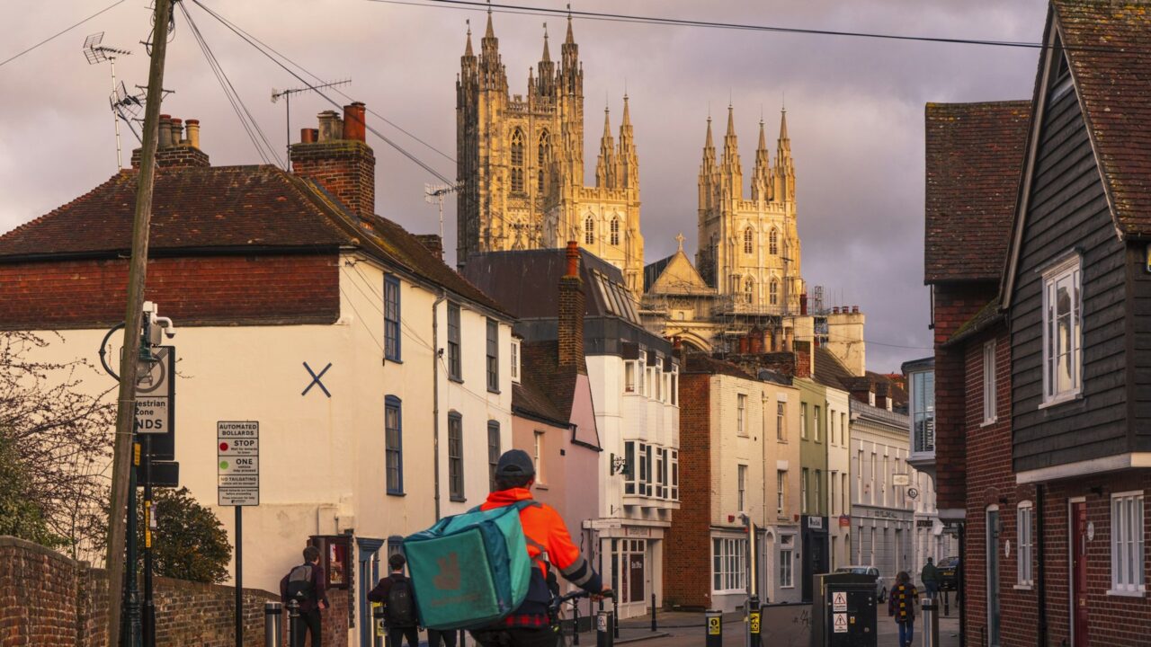 Person riding a scooter on a UK street with historic buildings in background