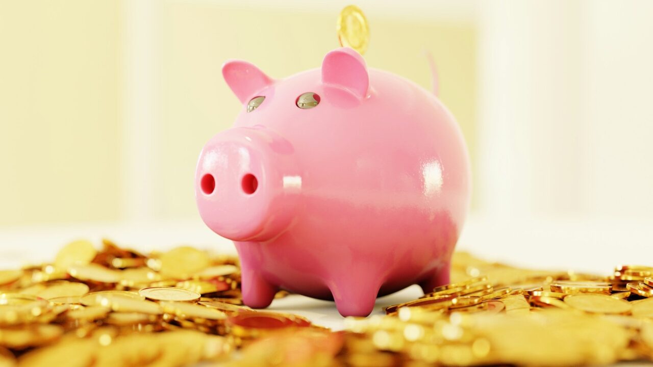 Pink piggy bank surrounded by scattered gold coins on a plain background
