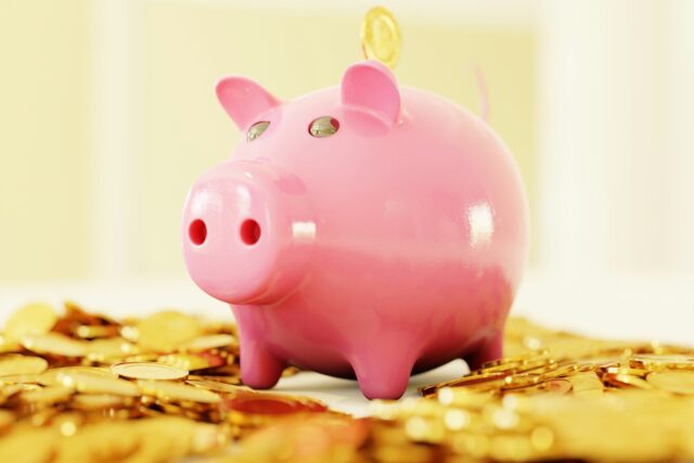 Pink piggy bank surrounded by scattered gold coins on a plain background
