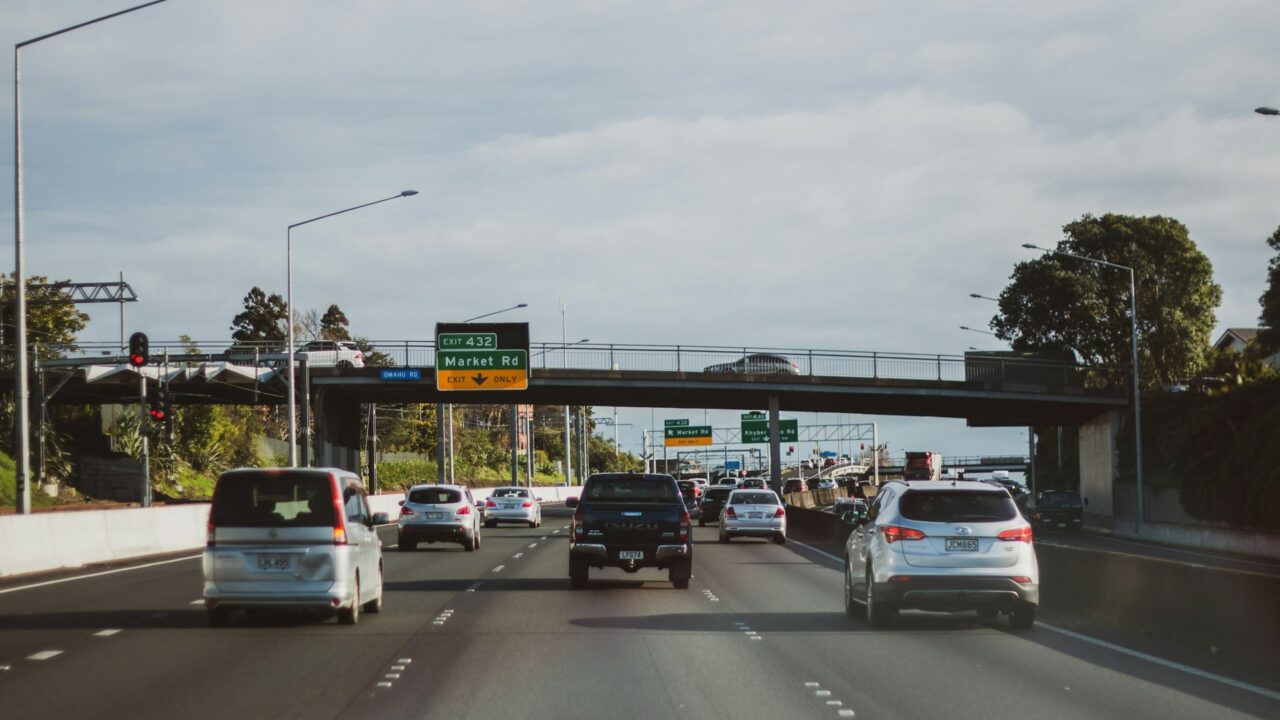 Multiple cars driving on a UK motorway with overhead gantry signs and road markings visible.