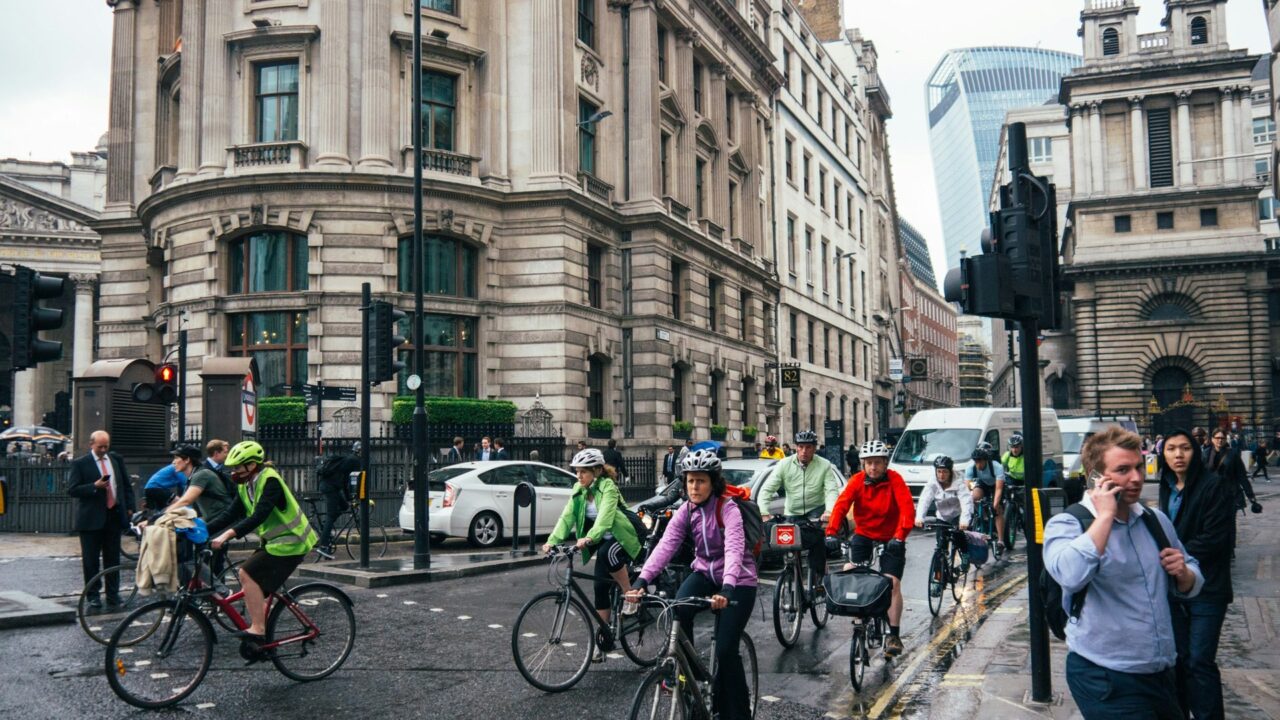 Multiple cyclists riding bikes on a city street with historic architecture in the background