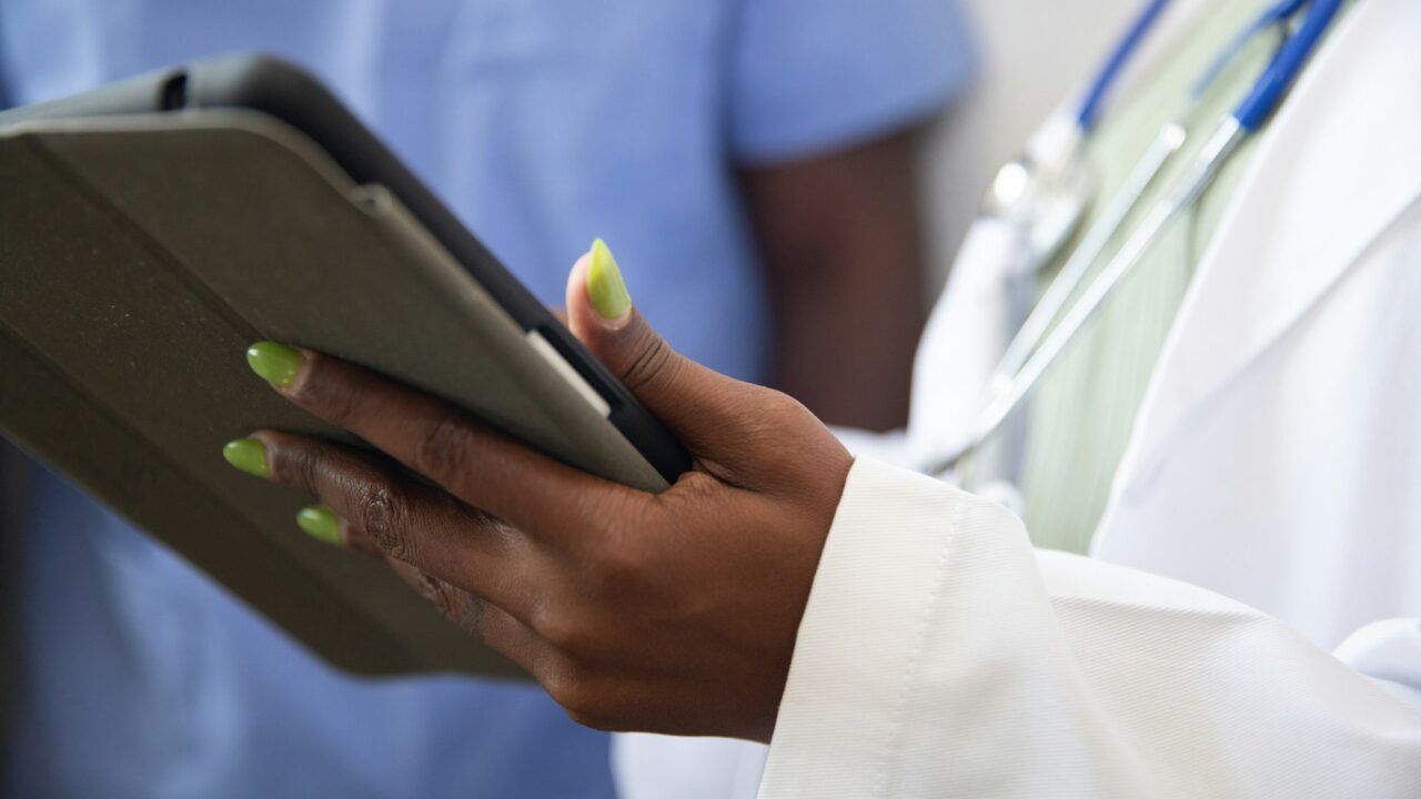 Doctor in white coat and stethoscope holding and using a tablet device