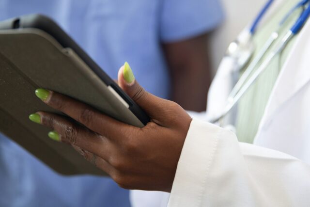 Doctor in white coat and stethoscope holding and using a tablet device