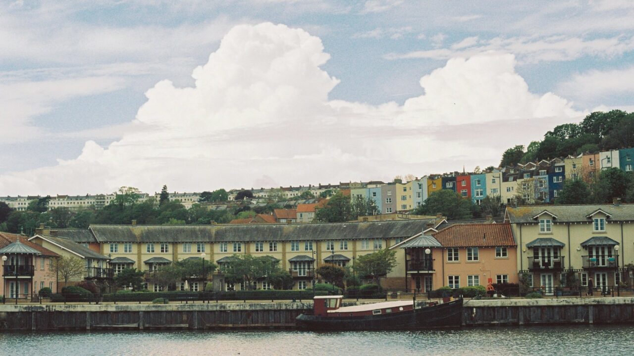 Colourful waterfront residential buildings reflected in calm water under blue sky with clouds