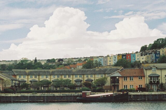 Colourful waterfront residential buildings reflected in calm water under blue sky with clouds