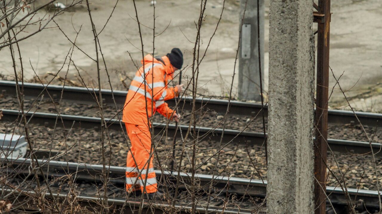 A railway worker in orange safety gear working on train tracks