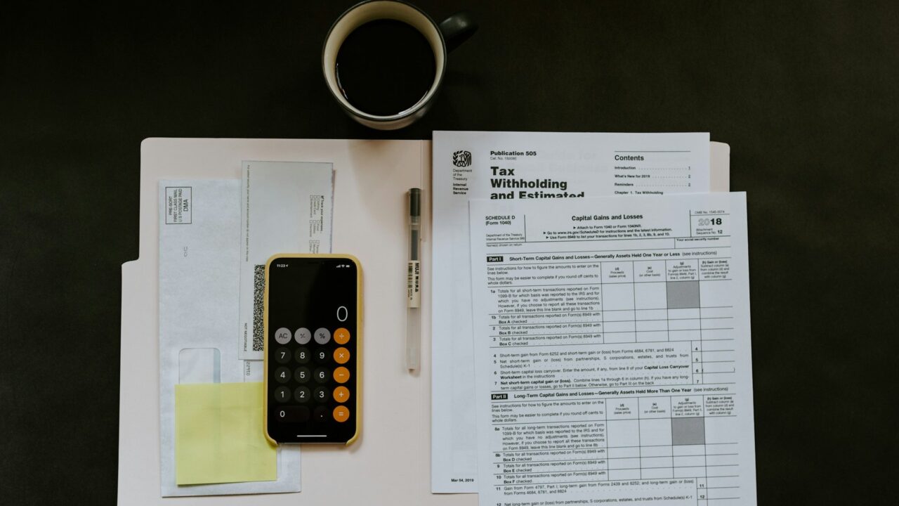 Black calculator, pen, and tax documents arranged on white papers against a dark background