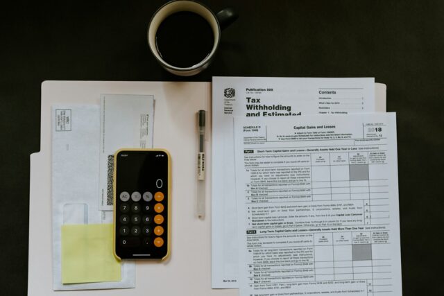 Black calculator, pen, and tax documents arranged on white papers against a dark background