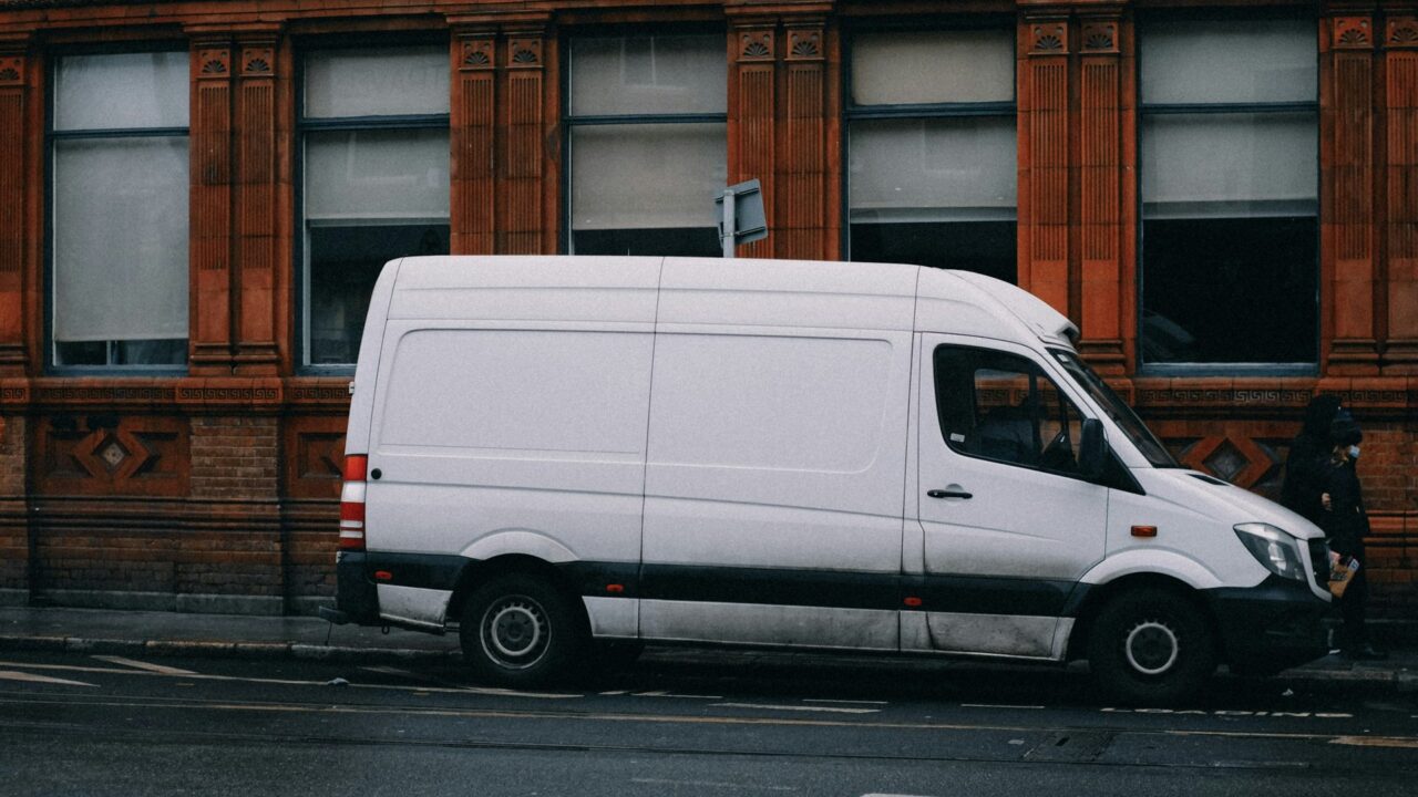 A white commercial van parked on a street in front of a brick building.