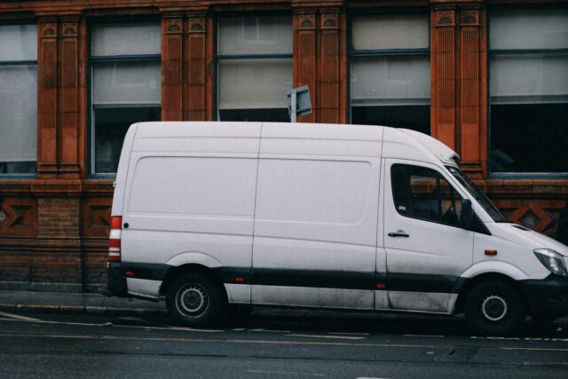 A white commercial van parked on a street in front of a brick building.