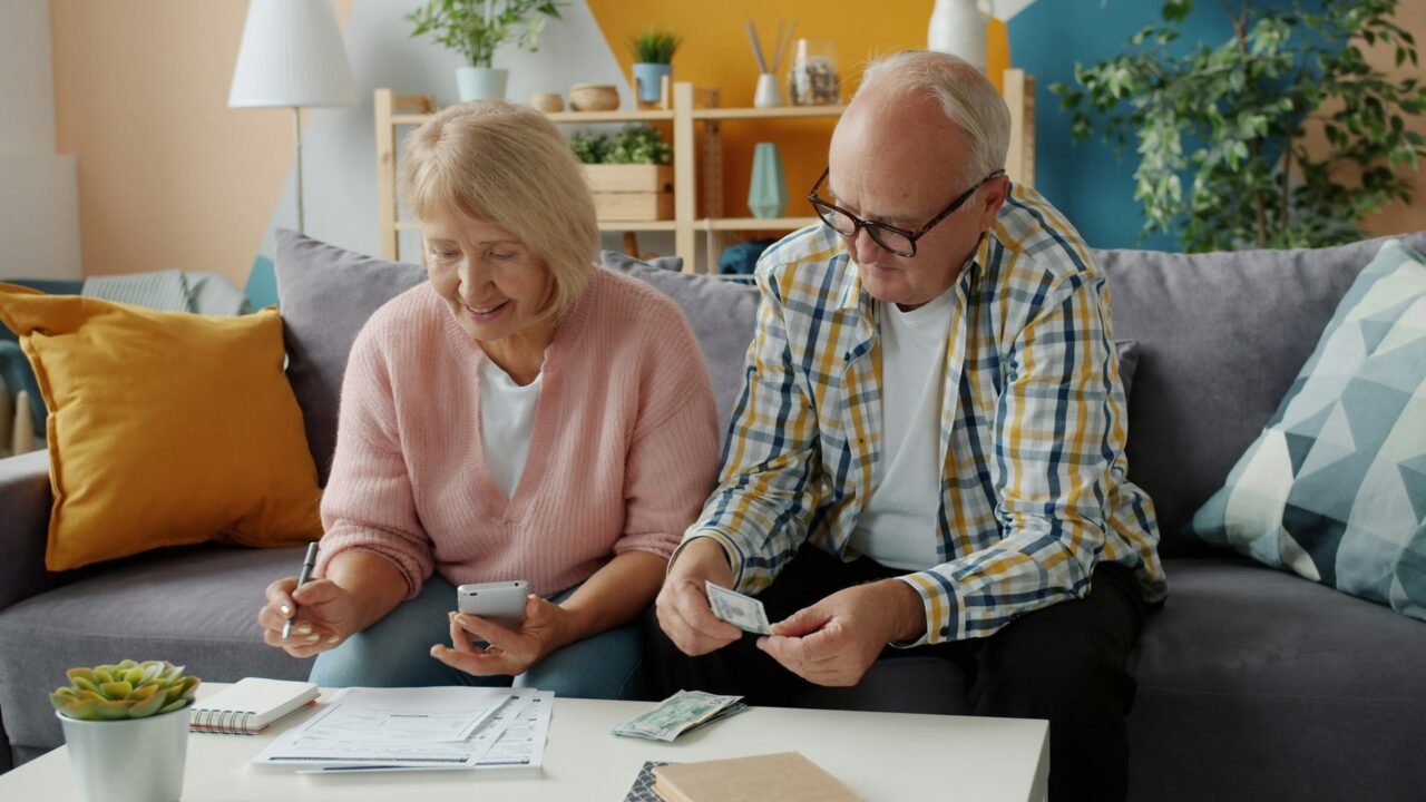 An elderly couple sitting on a sofa review financial documents together at home