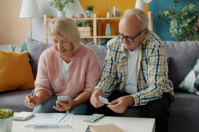 An elderly couple sitting on a sofa review financial documents together at home