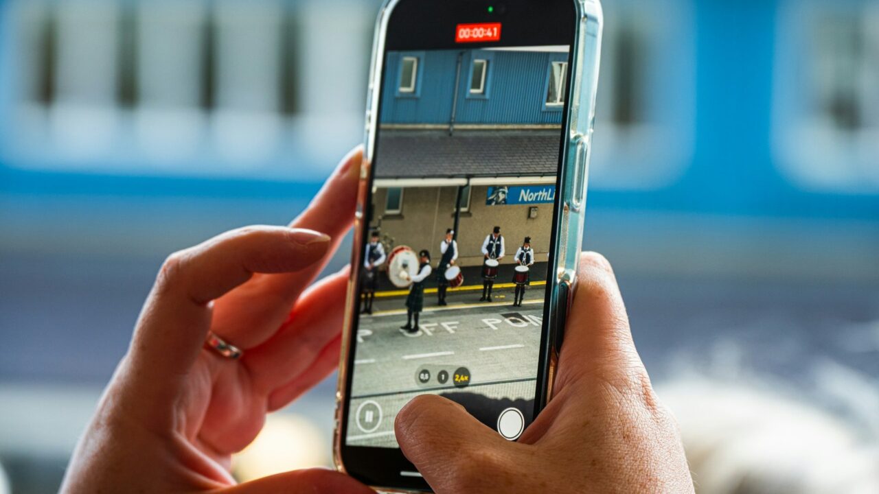 Hands holding a smartphone recording a subway platform with yellow safety line visible