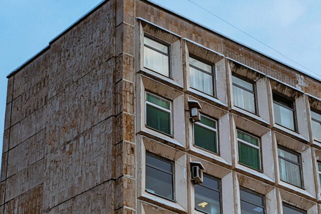 A multi-story residential building with weathered brown brick facade and regular window pattern showing signs of age and wear.