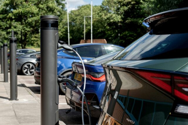Multiple electric cars charging simultaneously at a public charging station with trees in the background