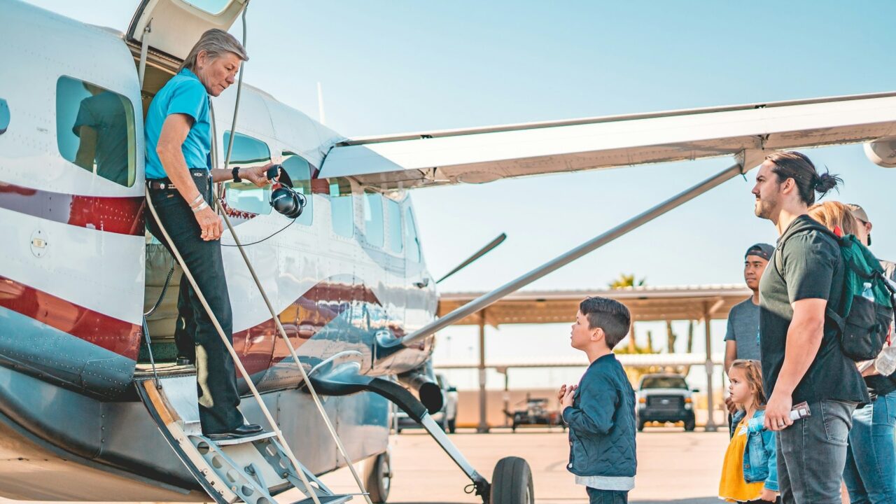 Group of people standing beside a small aircraft at an airport tarmac during daytime.
