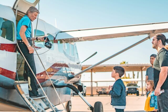 Group of people standing beside a small aircraft at an airport tarmac during daytime.
