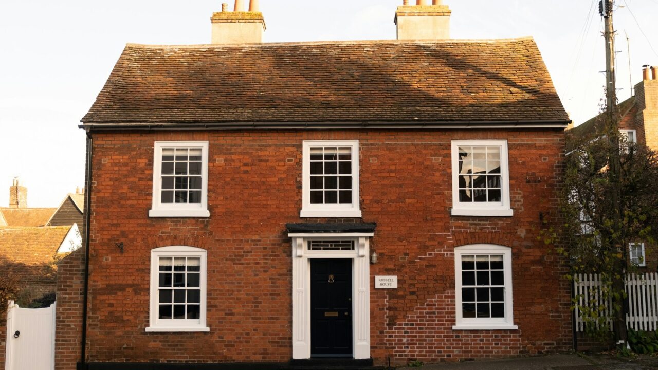 A red brick house with white-framed windows and a black front door, typical of British residential architecture.