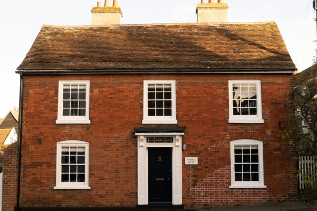 A red brick house with white-framed windows and a black front door, typical of British residential architecture.