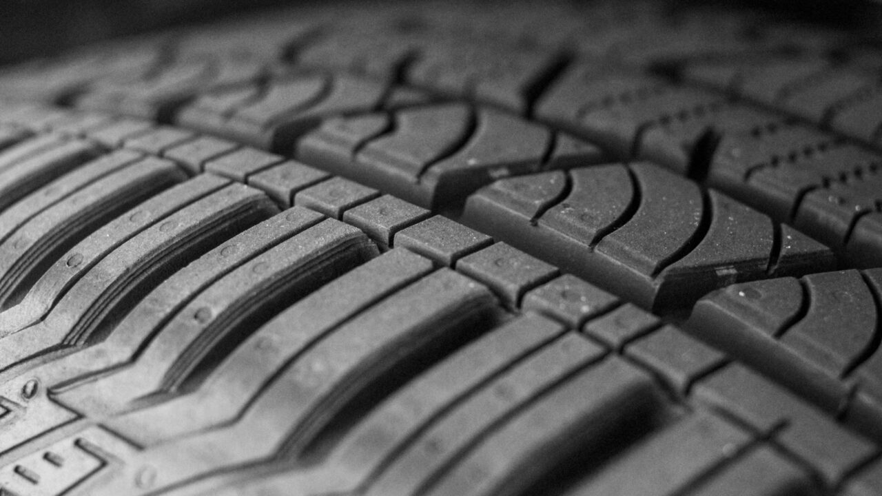 Close-up black and white photograph of a car tyre tread pattern showing the grooves and surface detail.