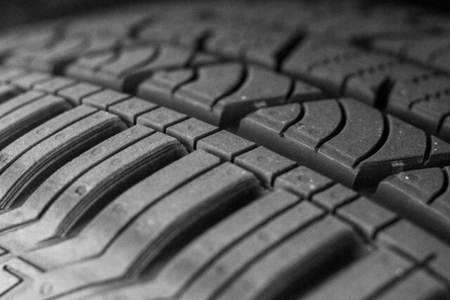 Close-up black and white photograph of a car tyre tread pattern showing the grooves and surface detail.