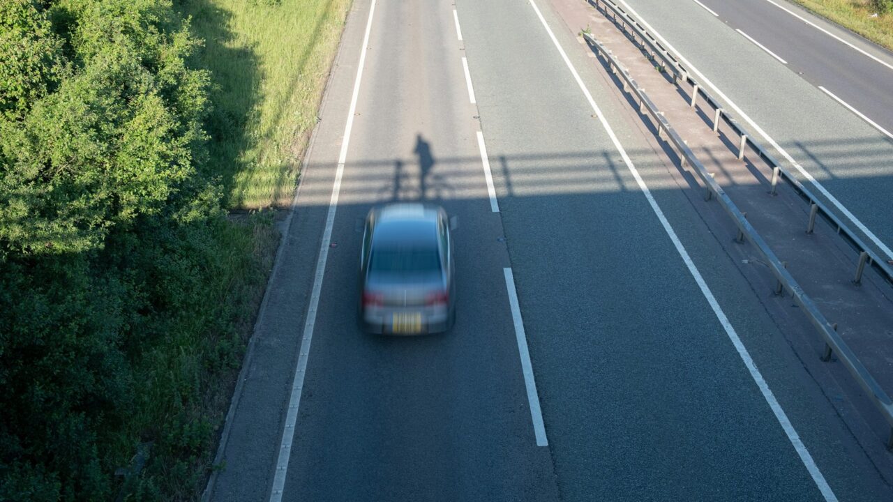 Aerial view of a car on a multi-lane motorway with green verges on either side